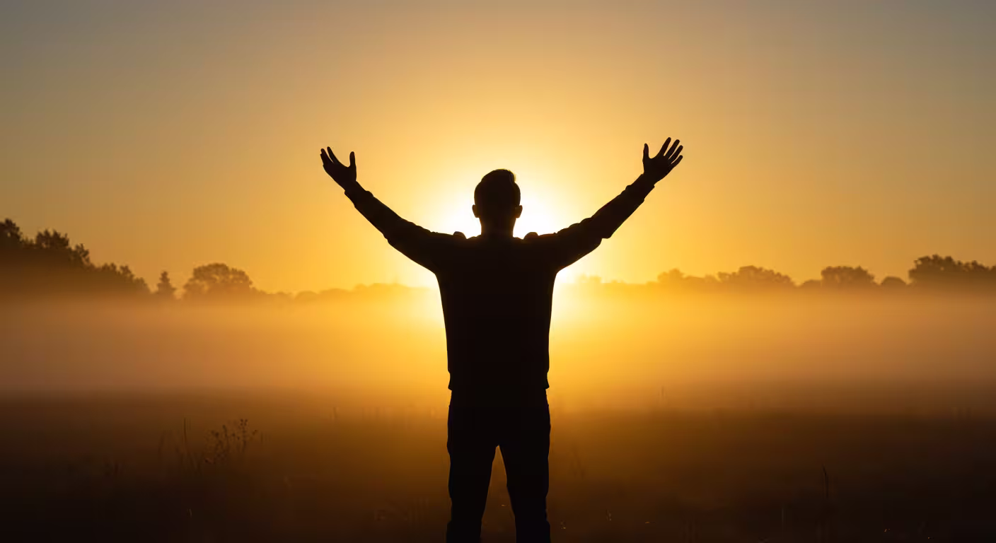 Homem com braços erguidos em um campo ao pôr do sol, simbolizando gratidão mesmo sem respostas concretas